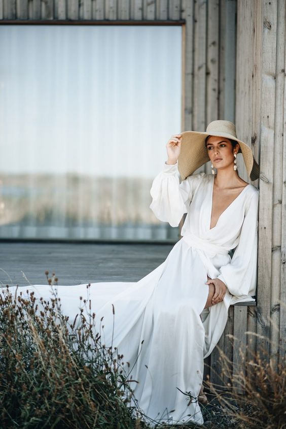 a beautiful destination bridal look with a flowy A-line wedding dress with a plunging neckline, statement earrings and a wide brim hat for a holiday feel
