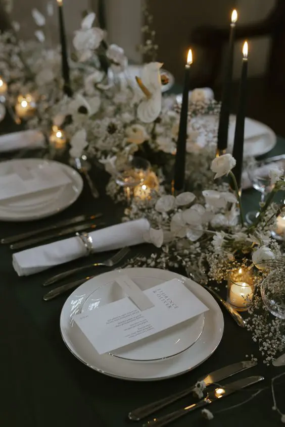 a beautiful wedding centerpiece of baby's breath, lunaria, orchids and tall and thin black candles looks heavenly chic and beautiful