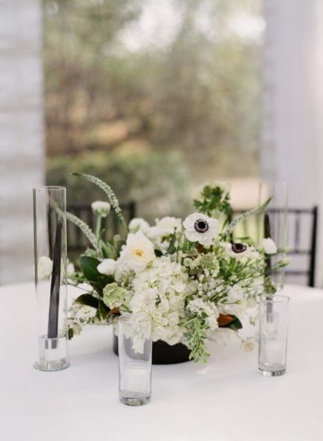 a black vase with various kinds of white blooms and some greenery plus candles around is a lovely and bold idea of a wedding centerpiece