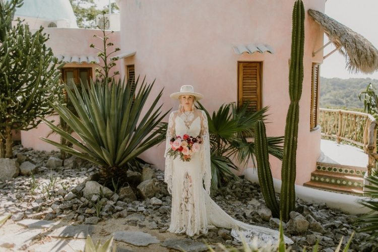 a boho Mexican bridal outfit with a gorgeous boho lace A-line wedding dress, bell sleeves and a train, a creamy hat and statement earrings