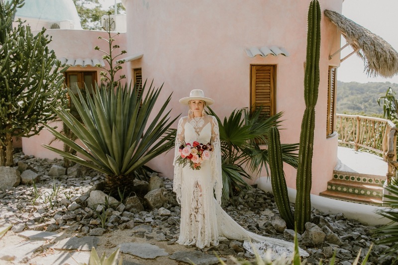 A boho Mexican bridal outfit with a gorgeous boho lace A line wedding dress, bell sleeves and a train, a creamy hat and statement earrings