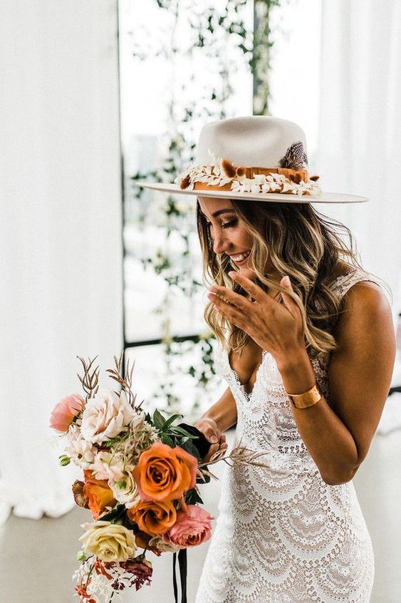 a boho bridal outfit with a boho lace fitting wedding dress with a deep neckline, a creamy hat with dried leaves and a statement bracelet