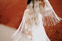 a boho bridal outfit with a boho lace wedding dress wiht long fringe and a black hat for a bold and contrasting touch