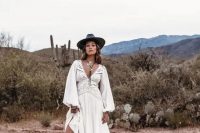 a boho bridal outfit with a gorgeous boho lace wedding dress with a train, a black hat, tall black cowgirl boots and statement accessories