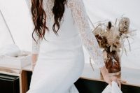 a boho bride wearing a boho lace fitting wedding dress with long sleeves and a high neckline, creamy hat with dried blooms and grasses