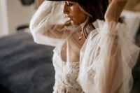 a boho destination bridal look with a semi sheer wedding dress with a lace bodice, sheer sleeves, a black hat with bold orchids