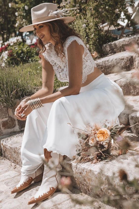 a boho western bridal look with a lace crop top, a plain midi skirt, cowboy boots and a nuetral hat decorated with dried grass