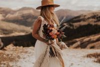 a boho western bridal look with an A-line wedding dress with a tulle skirt, a deep neckline and no sleeves, a beige hat and a cool colored bouquet