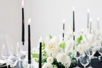 a chic and lovely wedding centerpiece of white blooms, greenery and tall and thin black candles is a gorgeous idea for a modern wedding