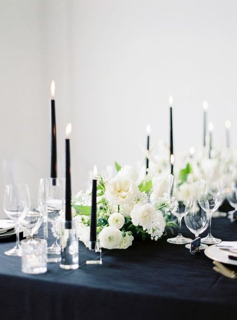 a chic and lovely wedding centerpiece of white blooms, greenery and tall and thin black candles is a gorgeous idea for a modern wedding