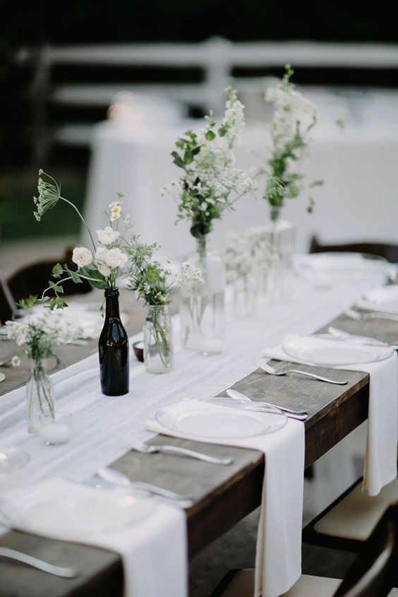 a cluster wedding centerpiece of clear and a black bottle, greenery and simple white blooms for a laid-back wedding