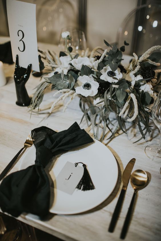 a delicate monochromatic wedding centerpiece of greenery, white anemones, grasses and a black table nimber holder is amazing