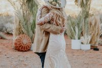 a desert boho bridal look with a lace applique A-line wedding dress with a train, a neutral hat with pastel blooms and greenery