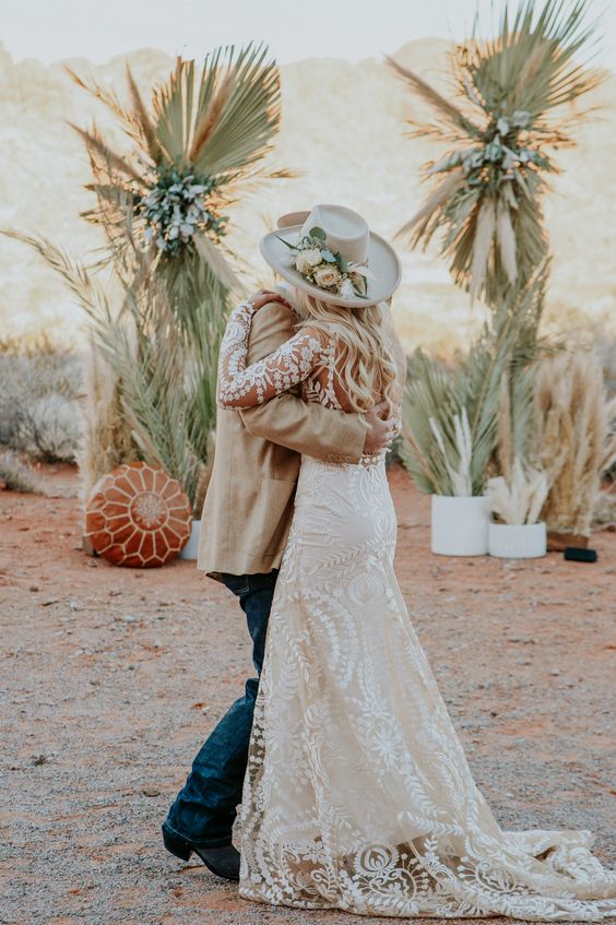 a desert boho bridal look with a lace applique A-line wedding dress with a train, a neutral hat with pastel blooms and greenery