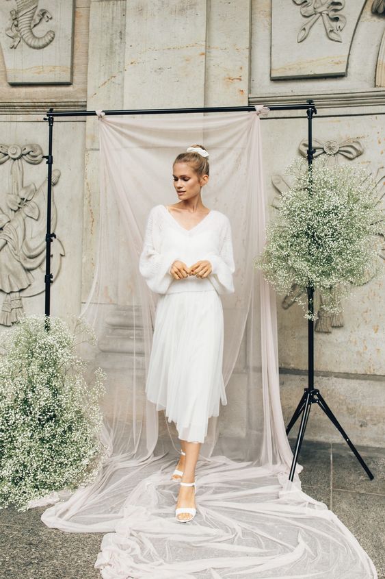a flowy oversized sweater with a deep V-neckline, a tulle midi skirt, white shoes and a top knot for a girlish yet casual winter bridal look