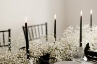 a gorgeous monochromatic wedding centerpiece of white baby’s breath, black candles in white candleholders is ideal for a minimalist wedding
