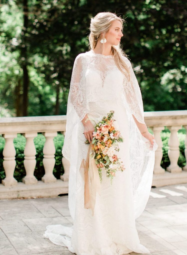 a lace A-line wedding dress paired with a matching lace capelet and delicate earrings for a strong Old World feel