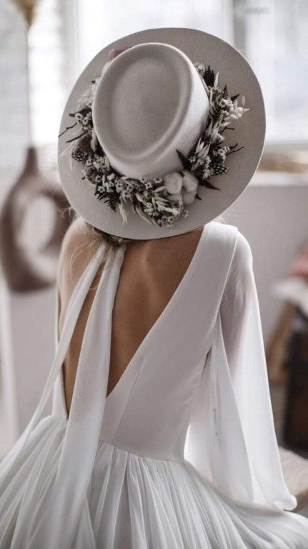 a modern and fresh bridal look with a plain white A-line wedding dress with a cutout back, a dove grey hat with blooms and greenery