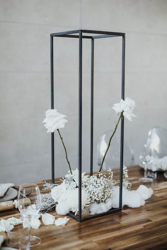 a modern black and white wedding centerpiece of white roses, baby's breath and a tall and thin black frame as a bold accent