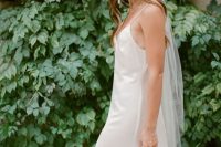 a modern bridal outfit with a silk slip wedding dress, a white hat with a veil and a beaded bag is an eye-catchy and chic idea