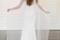 a modern plain mermaid wedding dress with a cutout back and a sheer pearly capelet with a train is a very girlish idea for a wedding