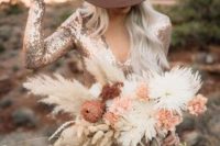 a pretty glam desert bridal look with a rose gold sequin wedding dress with a deep neckline and a brown hat plus a lush dried flower bouquet