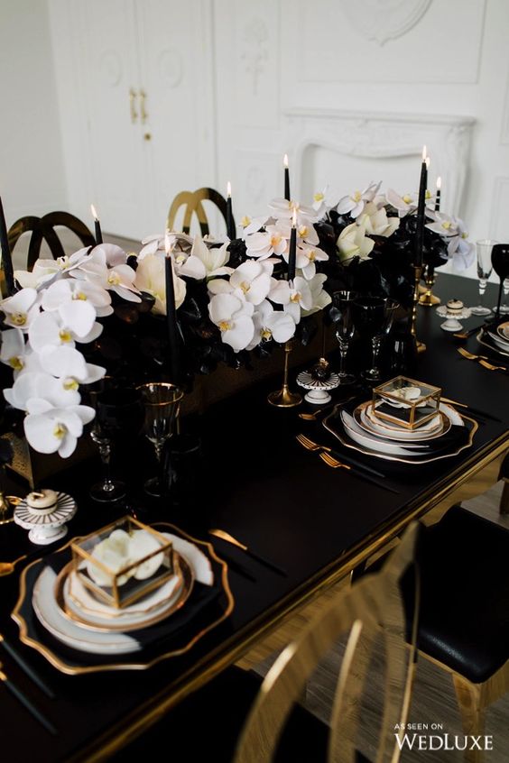 a refined black and white wedding centerpiece of black vases, white orchids, black calla liles, tall and thin black candles is wow