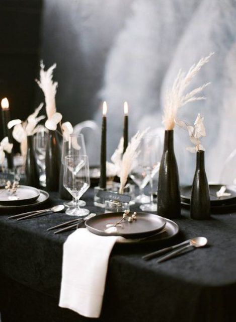 a refined modern black and white wedding centerpiece of black bottles, black candles, white dried blooms and grasses is a very lovely idea