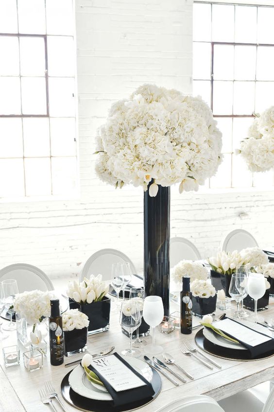 a refined modern wedding centerpiece of black vases with whie tulips, roses and hydrangeas plus candles around is a very stylish idea