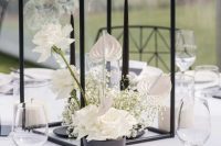 a refined wedding centerpiece of a black bowl with white roses, baby’s breath and orchids plus tall and thin black candles