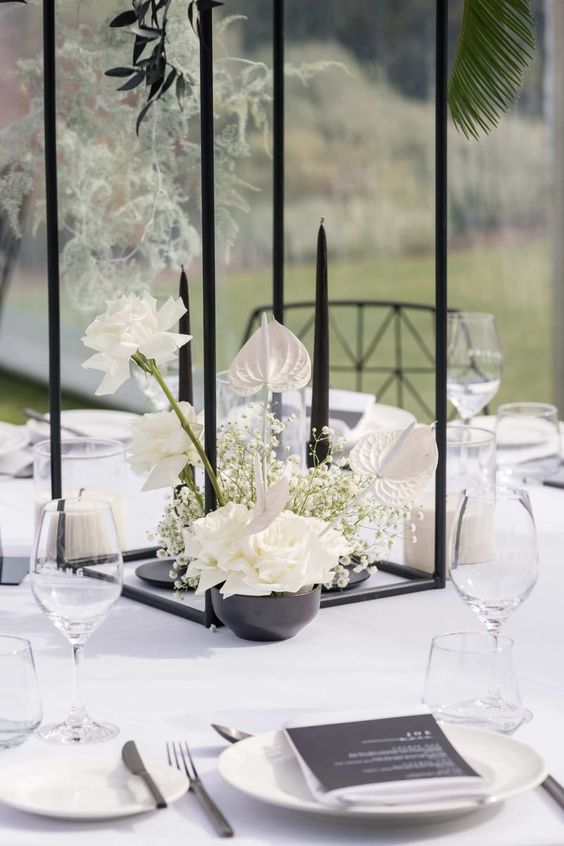 a refined wedding centerpiece of a black bowl with white roses, baby's breath and orchids plus tall and thin black candles