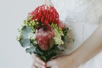 a small bright wedding bouquet of red proteas, greenery, berries and small white blooms-fillers is a catchy idea for a summer or fall wedding