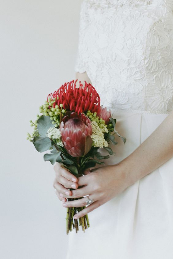 a small bright wedding bouquet of red proteas, greenery, berries and small white blooms-fillers is a catchy idea for a summer or fall wedding