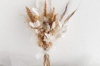 a small wedding bouquet of dried blooms, grass and leaves plus feathers is a very trendy solution for a fashion-forward bride