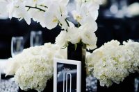 a sophisticated wedding centerpiece of black vases, white hydrangeas and orchids, a black and white table rnumber and candleholders