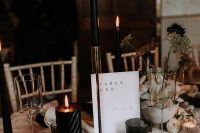 a sophisticated wedding centerpiece with pillar and tall and thin black candles, a white vase with black dried blooms