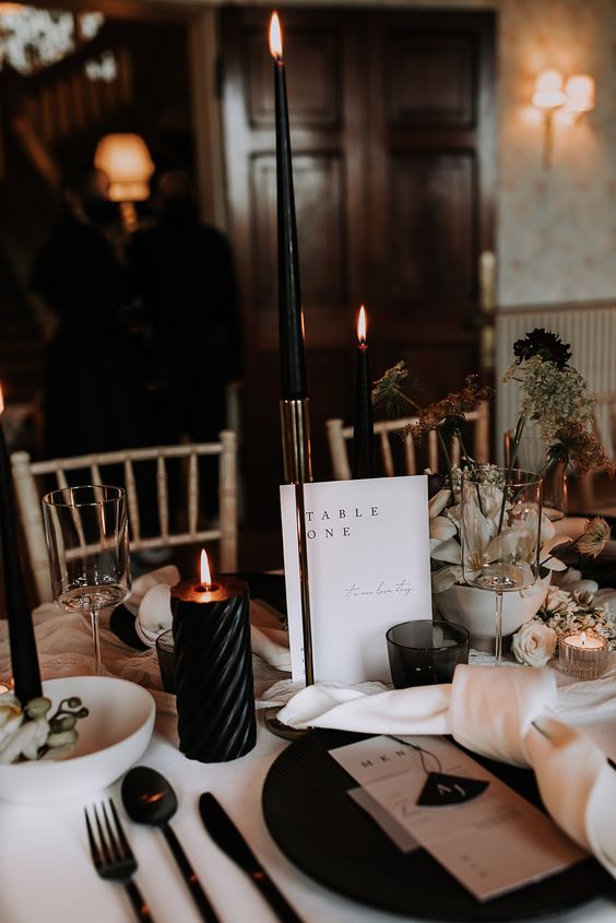 a sophisticated wedding centerpiece with pillar and tall and thin black candles, a white vase with black dried blooms
