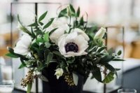 a stylish black and white wedding centerpiece of a black vase, anemones, greenery and some white candles around is pure elegance