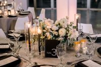 a stylish modern wedding centerpiece of white blooms, a black table number, tall and thin black candles and gilded candleholders is amazing