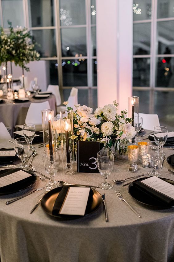 a stylish modern wedding centerpiece of white blooms, a black table number, tall and thin black candles and gilded candleholders is amazing
