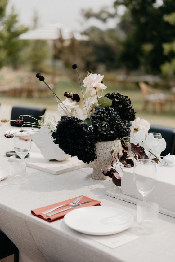 a whimsy wedding centerpiece of white, black, burgundy and blush blooms and a heavy stone vase will do for a modern wedding