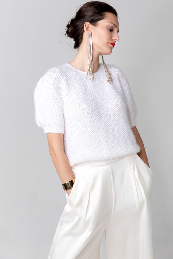 a white knit top with short sleeves, white high waisted wideleg trousers, statement silver earrings and a bracelet for a modern casual bridal look