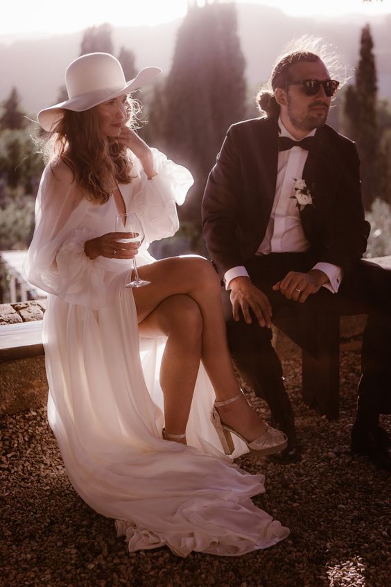 an elegant and whimsy bridal look with a flowy and semi sheer wedding dress, silver heels and a white hat is amazing