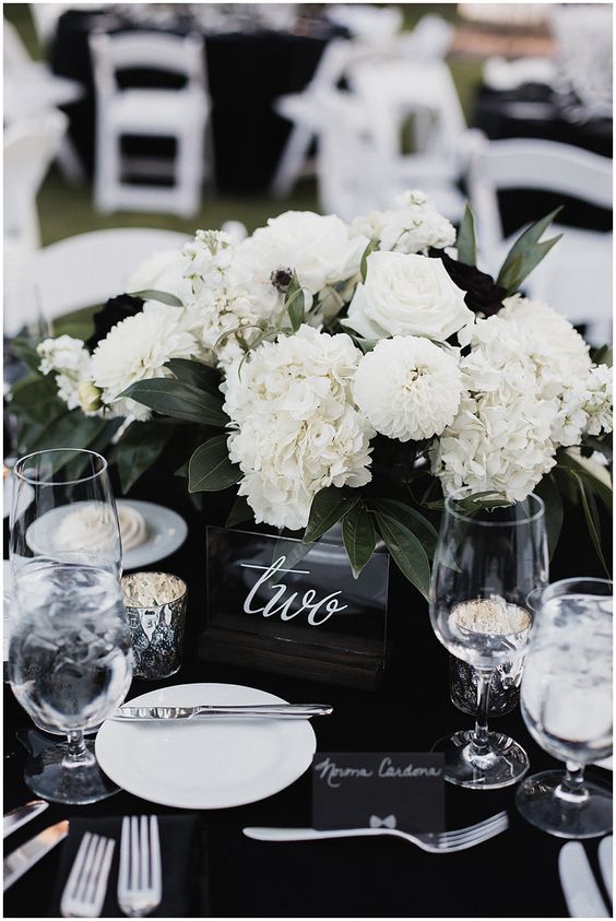 an elegant black and white wedding centerpiece of a black vase, white blooms and greenery and even a bit of black flowers