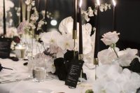 an elegant wedding centerpiece of white orchids and roses, tall and thin black candles and black linens plus black menus