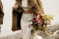 03 a boho bridal look with a two-piece wedding dress with lace, brown boots and a brown fur coat plus a lush and bold wedding bouquet
