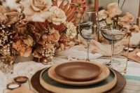 03 a refined and beautiful boho earthy wedding tablescape with a wooden placemat and brown and amber plates, rust and peachy blooms, copper candles and napkins