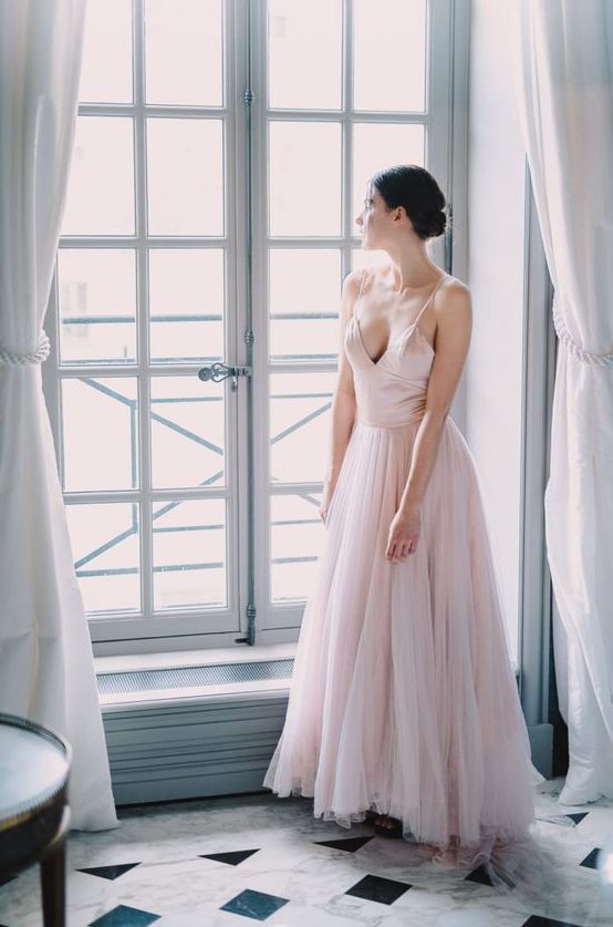 a blush wedding dress with a fitting silk bodice on spaghetti straps and a layered tulle skirt with train