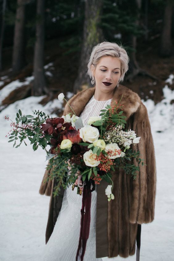 a brown fur coat, a dark lip and a moody wedding bouquet create a drama in this winter bridal look and add spice to it