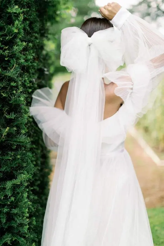 a fabulous off the shoulder wedding dress wiht a tulle ruffle neckline and an oversized tulel bow that matches and adds a girlish feel to the look